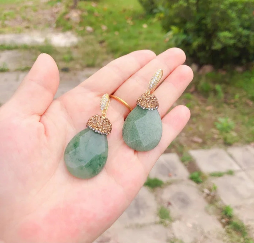 Amy Drop Earrings showcasing rhinestone-studded green crystal pendants in a hand, perfect for adding glamour.