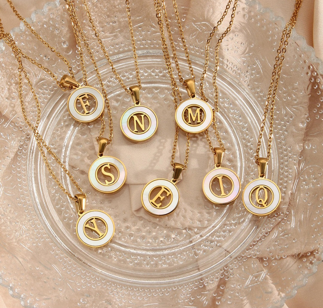 Collection of personalized initial necklaces featuring gold pendants with various initials on a decorative plate.