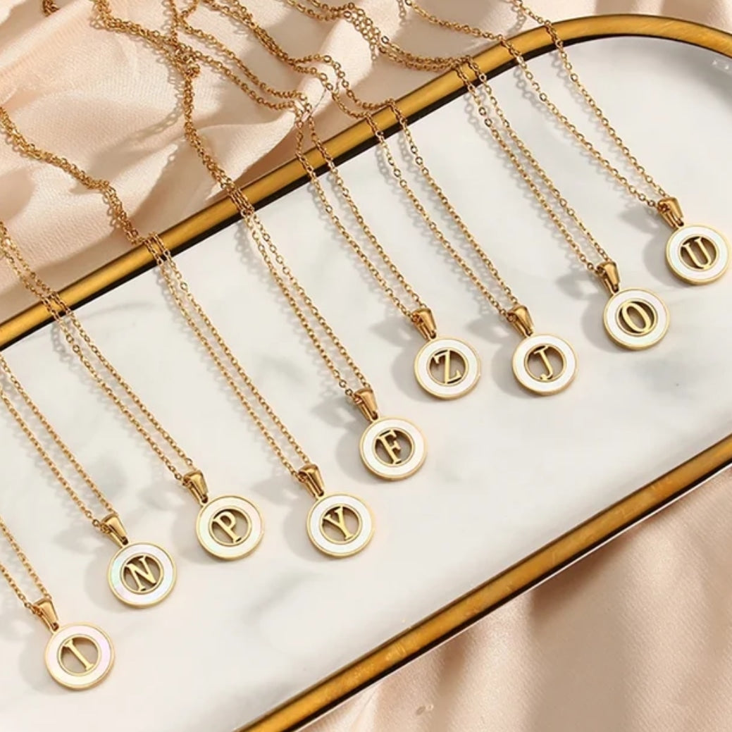 Personalized initial necklace display featuring various initials in gold plating on a stylish tray.